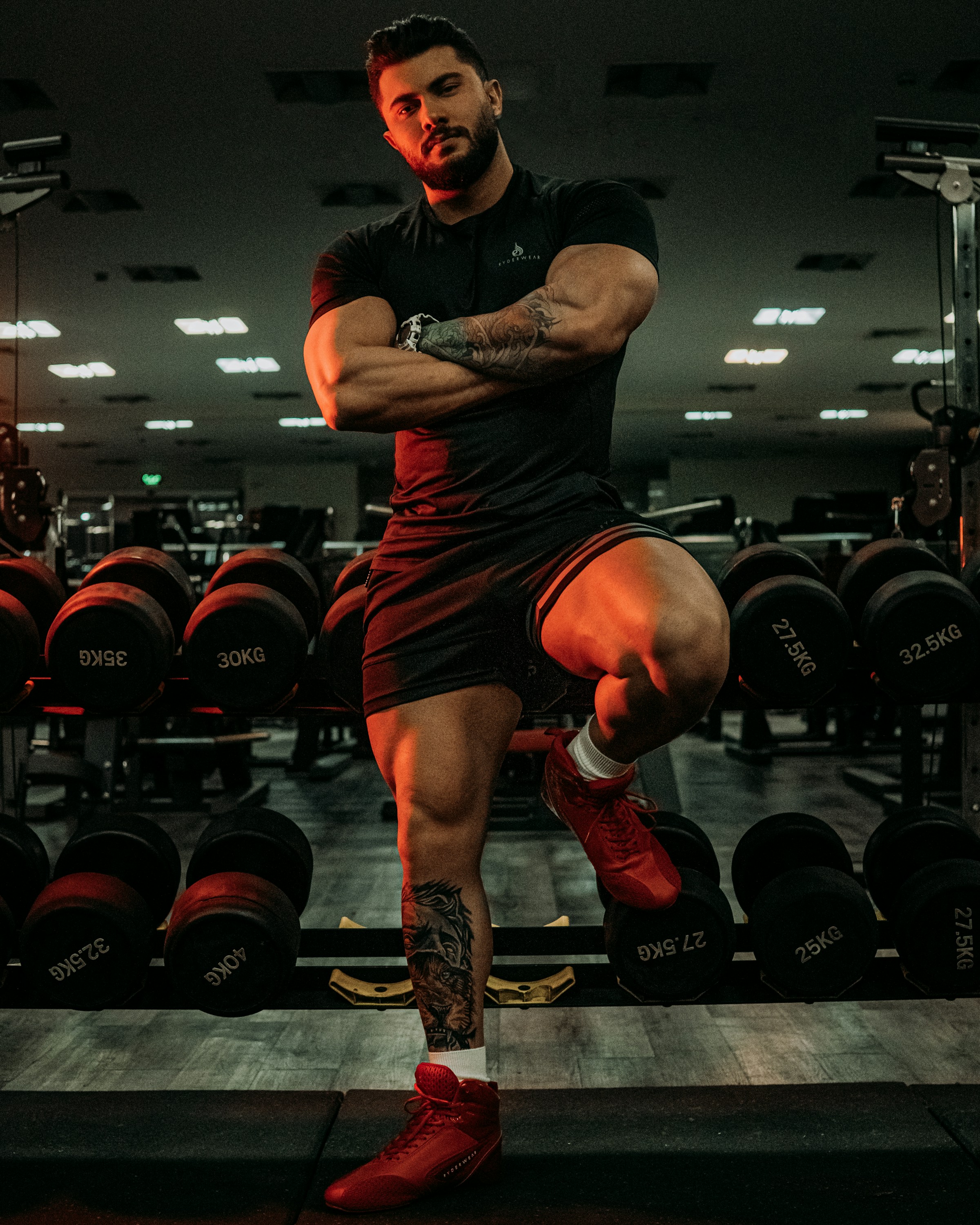 Strong man standing in the gym arms folded leaning on weight rack